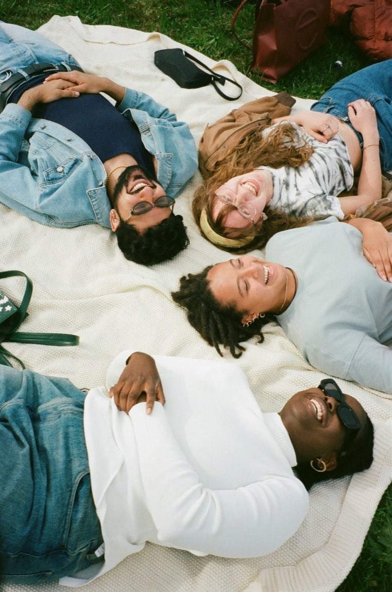 Four friends lying on a blanket in the grass, laughing together