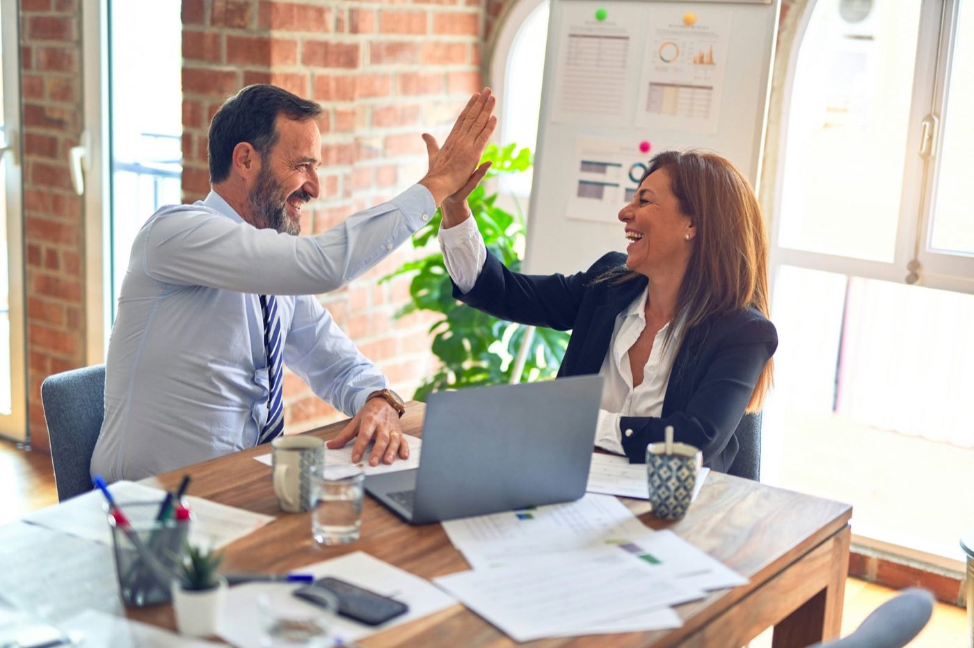 Two colleagues sharing a high five at a desk in a bright office
